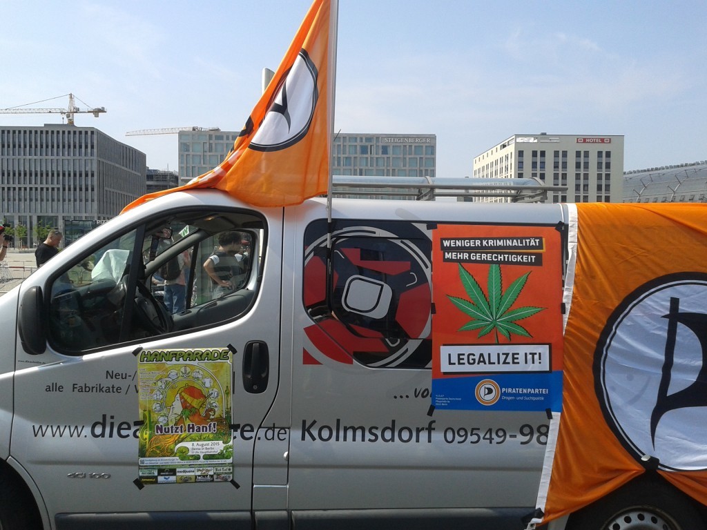 Der Demowagen der Piratenpartei von der Seite mit Flaggen und dem Plakat "Weniger Kriminalität - Mehr Gerechtigkeit - Legalize it"